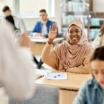 Eine glückliche, dunkelhäutige Frau hebt im Sprachkurs der Volkshochschule die Hand.