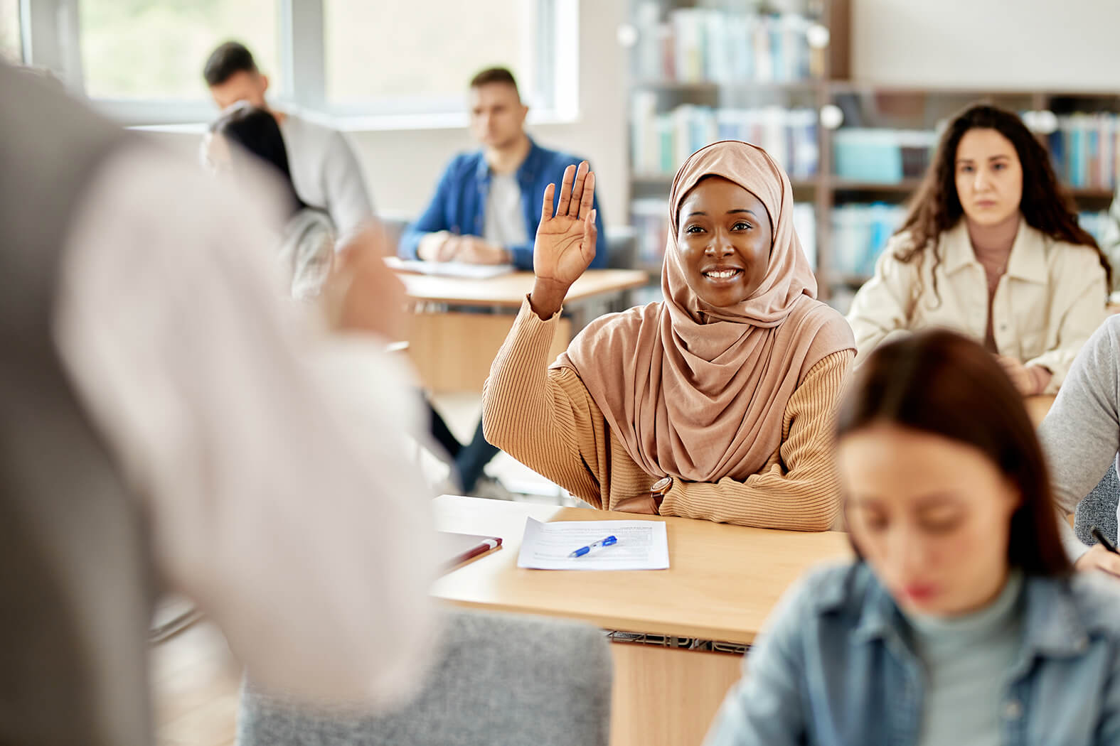 Eine glückliche, dunkelhäutige Frau hebt im Sprachkurs der Volkshochschule die Hand.