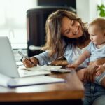 Frau arbeitet mit Baby auf dem Schoß in Wohnzimmer